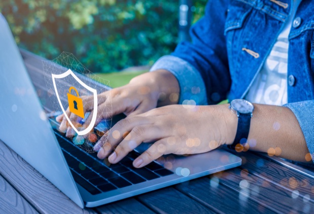 Person typing on a laptop with a shield and padlock security overlay