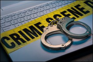 Handcuffs on a laptop keyboard beside crime scene tape.