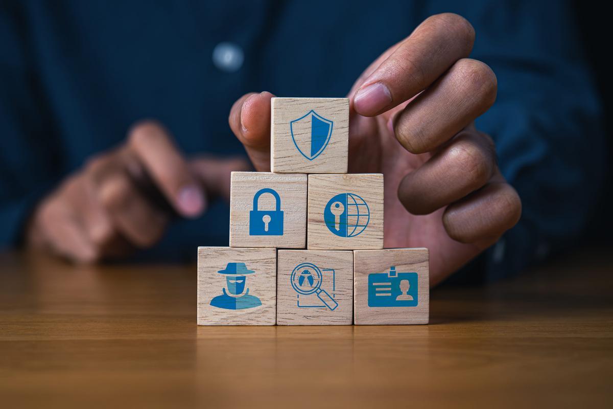 Person stacking wooden blocks printed with padlock, shield, and identity symbols.