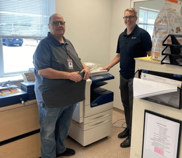 iTech technicians and customer standing in front of a printer, showcasing professional support to help your business run efficiently.